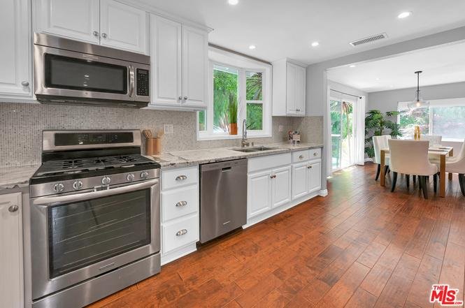 Kitchen with stainless steel appliances, white cabinets, wood floor, window, and dining area.