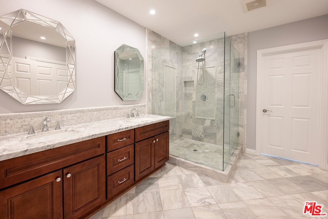 Bathroom with double sinks, dark wood cabinets, glass shower, and marble floor.