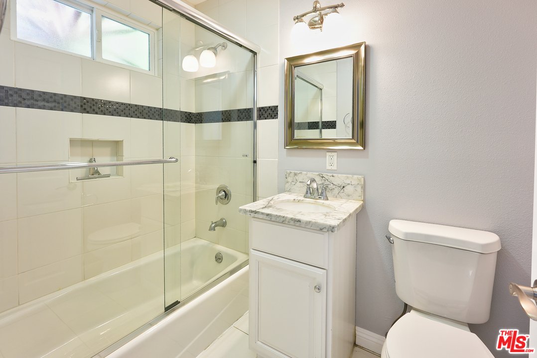 Bathroom with glass shower, bath tub, sink counter, toilet, mirror, and window.