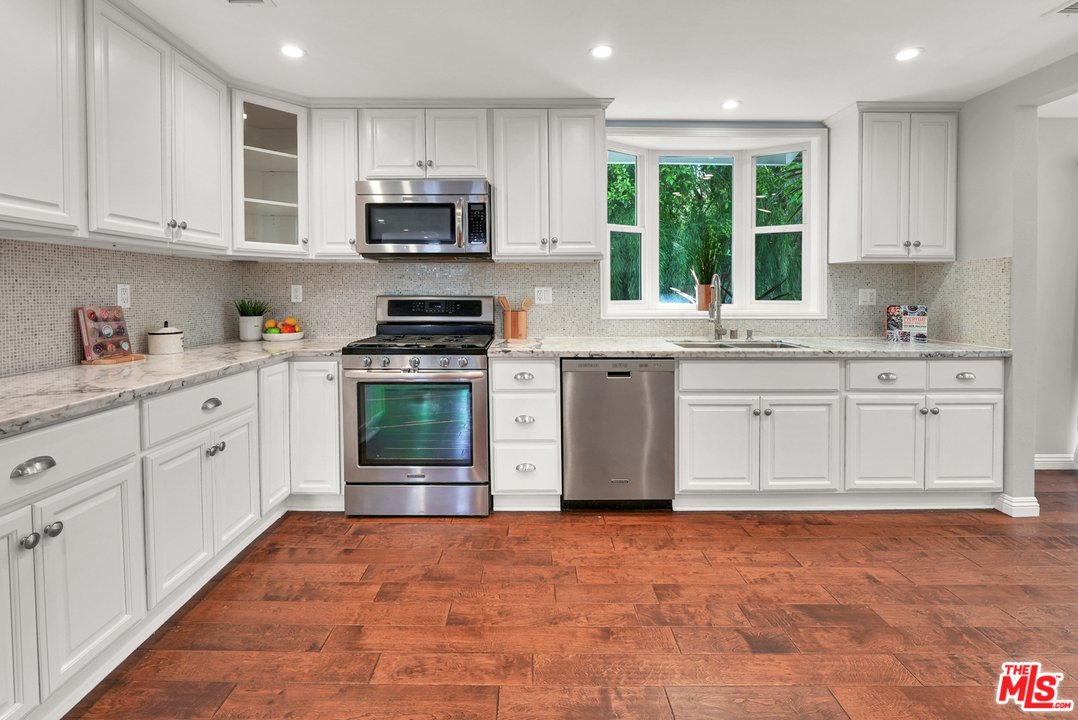 Kitchen with white cabinets, stainless steel appliances, granite counter, wood floor, and window.