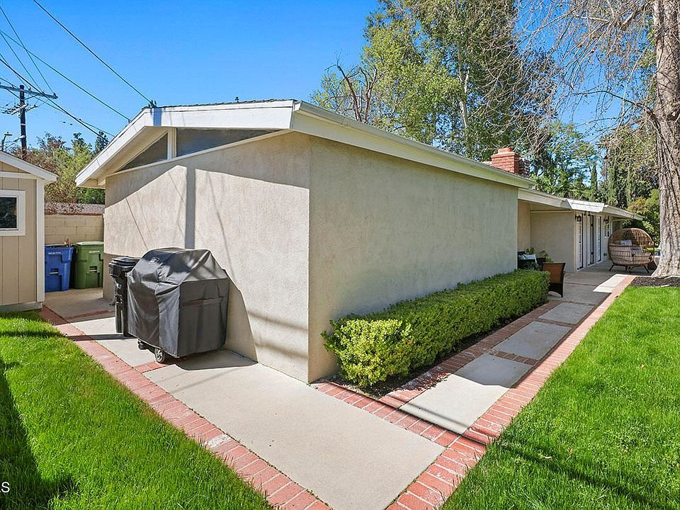 Side of house with yard, concrete path, green plants, and outdoor grill California real estate.