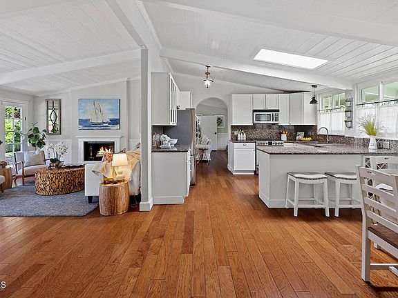 Kitchen with large island, appliances, open layout to living room with seats and fireplace, and wood floor.