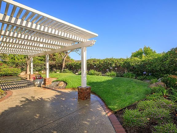 California real estate house patio with white pergola, green lawn, and plants.