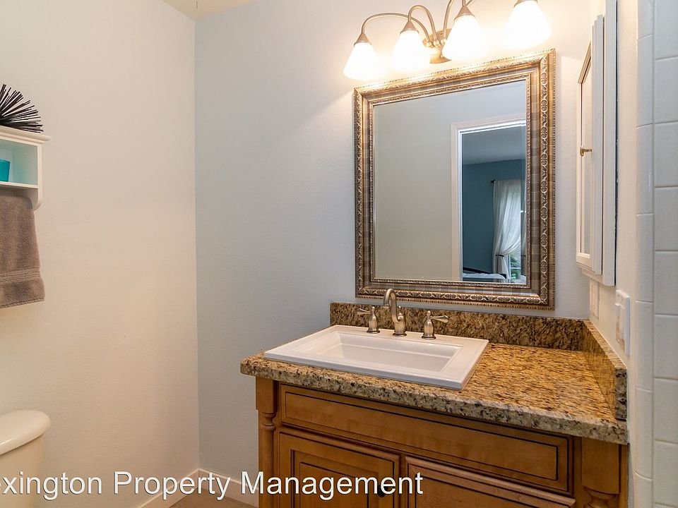Bathroom with sink, granite countertop, decorative mirror, wall lights, towels, and cabinets