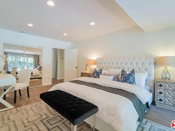 Bedroom with bed, pillows, bench, bedside lamps, and mirrored wardrobe.