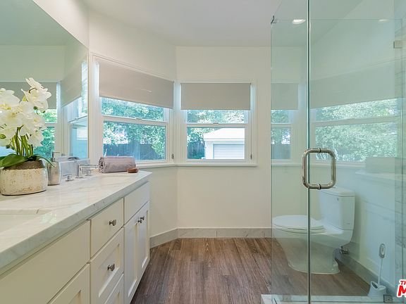 Bathroom with glass shower, toilet, double sink vanity, cabinets, and plants.