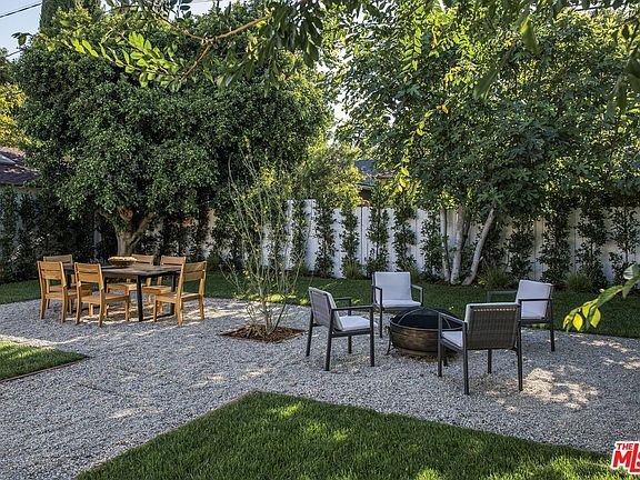 Backyard with gravel path, wooden dining table, chairs, and fire pit with seating