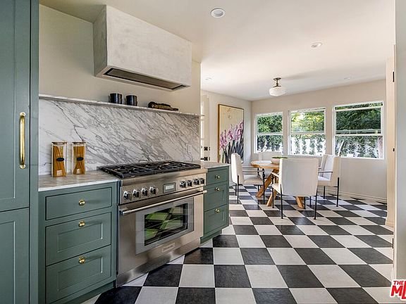 Kitchen with marble backsplash, green cabinets, modern appliances, checkered floor, dining area with white chairs, and large windows