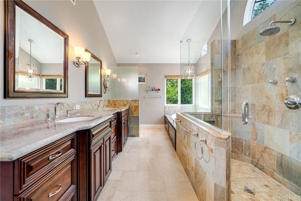 Bathroom with double sinks, dark wood cabinets, bath tub, glass shower, tiles, and window.
